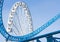 Ferris wheel and Loop turn on a blue roller coaster in an amusement park.