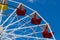 Ferris wheel with yellow and red bowls against blue sky with thin clouds