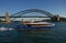 Ferry cruising in water in front of iconic Sydney Harbor Bridge. Urban coastal cityscape with ferryboats and historic landmark.