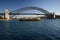 Ferry cruising in water in front of iconic Sydney Harbor Bridge. Urban coastal cityscape with ferryboats and historic landmark.