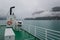 Ferry deck view to the fjord mountains in clouds and fog.