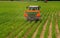 Fertiliser spreader machine trailed by tractor on a field with young corn plants