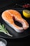 Fesh raw salmon fillet with herbs, on black wooden surface