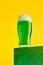 Festival drink. Glass of foamy frothy green beer over bright yellow background. Traditional taste. Concept of st