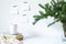 Festive breakfast still life.Cup of coffee, books and vase with fir branches.Empty notepads mockup hanging on the white wall.