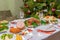 Festive Christmas served table against beautiful green pine tree decorated with many colorful new year toys. Xmas dinner,