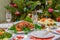 Festive Christmas served table against beautiful green pine tree decorated with many colorful new year toys. Xmas dinner,
