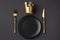 Festive creative royal table setting on a dark background. Gold crown, fork and knife. Valentine`s Day, Wedding Day, Birthday,