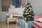 Festive decorated fir-tree in living room with piano, pink sofa and wrapped Christmas gifts. Tender color palette in interior