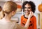 Festive makeup for Halloween. Woman doing pumpkin make-up for ethnic curly boy in costume while preparing holiday