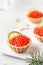 Festive New Year appetizer tartlets stuffed with red caviar and a slice of lime close up on a white tray with text space
