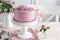 Festive pink cake on white cake stand decorated with fresh roses for Valentines Day