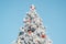 Festive snowy decorated Christmas tree against clear blue sky, outdoors. Merry christmas celebration and happy new year concept