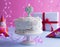 A festive sponge cake with white cream for a birthday, on a pink and blue background. Tinsel, waverki and boxes of gifts. Question