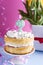 A festive sponge cake with white cream for a birthday, on a pink and blue background. Tinsel, waverki and boxes of gifts. Question