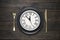 Festive table setting with black dish, clock, knife and fork on dark wooden table. New Year table setting