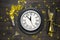 Festive table setting with black dish, clock, wine glass and gold confetti decoration on dark wooden table