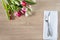 Festive table setting with bunch of purple tulips and forged fork and knife on white napkin and wooden background