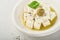 Feta cheese cubes with rosemary, olives and olive oil sauce in white bowl on light gray background. Traditional Greek homemade