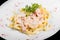 Fettuccine pasta with meat, cream sauce and herbs, in bowl isolated on black background.
