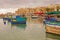 Few colourful traditional Maltese fishing boats Luzzu docking with old houses behind at cloudy fishing village Marsaxlokk, Malta
