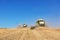 A few combines cutting a swath through the middle of a wheat field during harvest