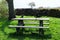 Few jackdaws birds fight for food on the wooden table and bench in the park with stone fence on the background