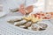 A few oysters with a sliced lemon on a large dish in the foreground with a man who holds an oyster in the background.