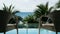 FHD. Zoom out of two relaxing vacation chair in front of swimming pool near the beach with coconut palm tree and sea view