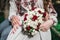 Fiance and the bride hold in hand wedding bouquet of biege and red roses.