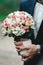 Fiance in a dark blue suit holds a wedding bouquet made of white flowers