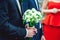 Fiance in a dark blue suit holds a wedding bouquet made of white flowers