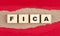 FICA word on wooden cubes on red torn paper , financial concept background