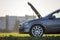 Fictional non existent modified image of a car. Car with open hood on empty gravel field road on blurred bright sky copy space