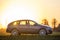 Fictional non existent modified image of a car. Gray car parked in countryside on blurred rural landscape and orange sky at sunset