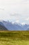 Field and distant snowy mountains. South Island landscapes on the way to Milford Sound. Fiordland National Park. New Zealand