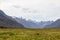 Field and distant snowy mountains. South Island landscapes on the way to Milford Sound. Fiordland. New Zealand