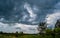 A field of green trees and a sky full of black, threatening clouds. Strong storm begins