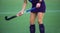 Field hockey player, in possesion of the ball, running over an astroturf pitch, looking for a team mate to pass to