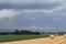 A field with round straw bales next to a field with potatoes and a grey sky in the background in holland