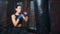 Fierce Asian fit woman with wrapped hands practicing kickboxing on punching bag at box studio