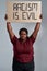Fierce plus size young african american woman in casual clothes looking at camera, holding Racism is evil banner above