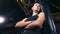 Fierce young kickboxer brunette girl posing with crossed hand at dark boxing gym low angle