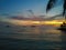 Fiery glow sunset over a beautiful tropical beach and ocean water. Different colours of clouds and the silhouette of palm tree.