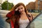 With fiery red locks and a beaming smile, the young woman wearing poses beside red car