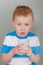 Fiery redhead young boy in blue and white stripped shirt holding a glass of milk. Portrait format on grey with copy space.