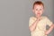 Fiery redhead young boy in yellow shirt in finger to chin in deep thought stance. Landscape on grey background with copy space.