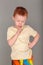 Fiery redhead young boy in yellow shirt in finger to chin in deep thought stance. Portrait format on grey with copy space above.