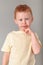 Fiery redhead young boy in yellow shirt in fist to chin in deep thought stance. Portrait format on grey background with copy space