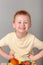 Fiery redhead young boy in yellow shirt fists on hips sitting on a stool with a huge cheeky grin. Portrait on grey background.